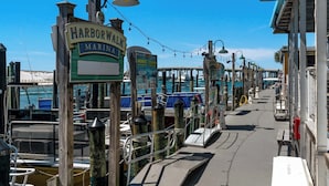 Eine Marina mit angestaubten Booten, einem Schild mit der Aufschrift "Harbor Walk Marina" und einer Holzpromenade, die zum Wasser führt.