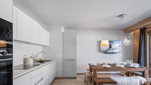 A modern kitchen with white cabinetry, a built-in oven, and a dining area with a wooden table and benches. - Luxury 3-bedroom apartment in Megève with pool and gym (Megève)