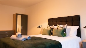 Una cama bien hecha con un cabecero oscuro, un armario de madera y un espejo en la pared.