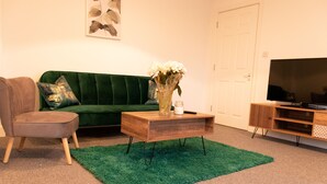 Una sala de estar con un sofá verde, una mesa de centro de madera, un tapete verde, un televisor y un mueble.