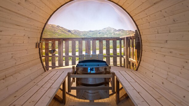 A wooden cabin with a circular window, a hot tub, and a wooden deck with a view of mountains. - Spacious apartment 6 pers, terrace sauna close to slopes (Val Thorens)