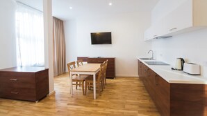 A modern kitchen with wooden cabinets, a dining table with chairs, a flat-screen TV mounted on the wall, and a coffee maker on the counter. - Apartamenty Swinoujscie - Rubin I (Swinoujscie)