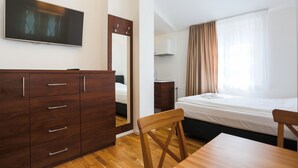 A hotel room with a bed, a wooden dresser, a chair, a table, a TV, and a window with curtains. - Apartamenty Swinoujscie - Rubin I (Swinoujscie)