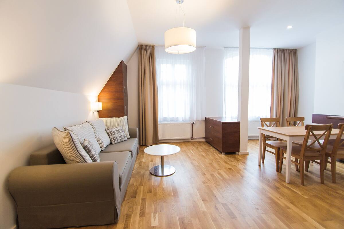 Ein modernes Wohnzimmer mit einer Couch, einem runden Couchtisch, einem Esstisch mit Stühlen und einer Pendelleuchte.