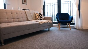 Uma sala de estar moderna com um sofá cinzento, uma poltrona azul e uma varanda com guarda-corrimão.