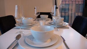 Mesa de jantar posta com tigelas, pratos e talheres brancos, com copos de vinho e uma colher à vista.