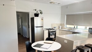 A modern kitchen with a central island, a refrigerator, a stove, and a sink. There are two black chairs around a small table with a notebook. - Farmstay Cottage on the Strathbogie Tablelands. (Boho South)