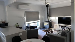 A modern living room with a flat-screen TV, a ceiling fan, and a fireplace. - Farmstay Cottage on the Strathbogie Tablelands. (Boho South)