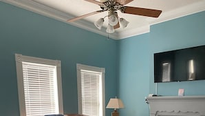A living room with a brown leather couch, a glass coffee table, a fireplace, and a ceiling fan.