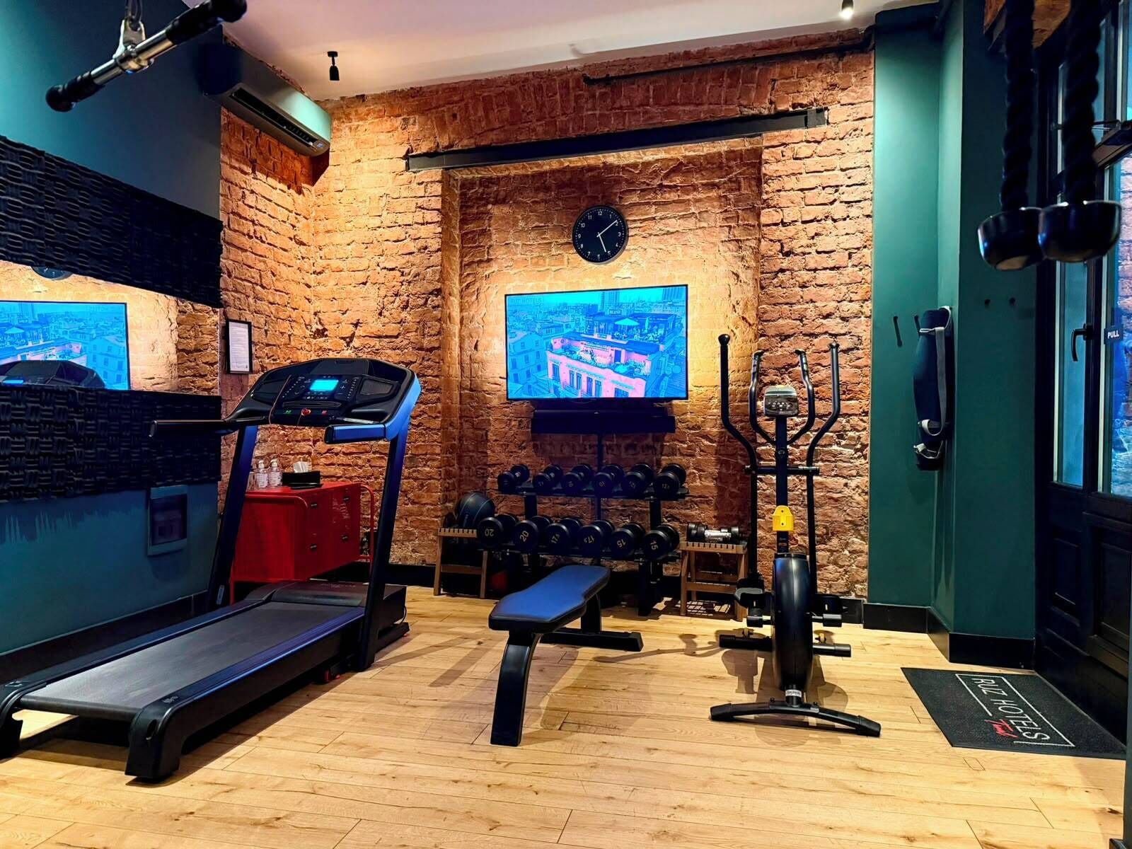 A gym with a treadmill, weights, and a TV screen displaying a cityscape.