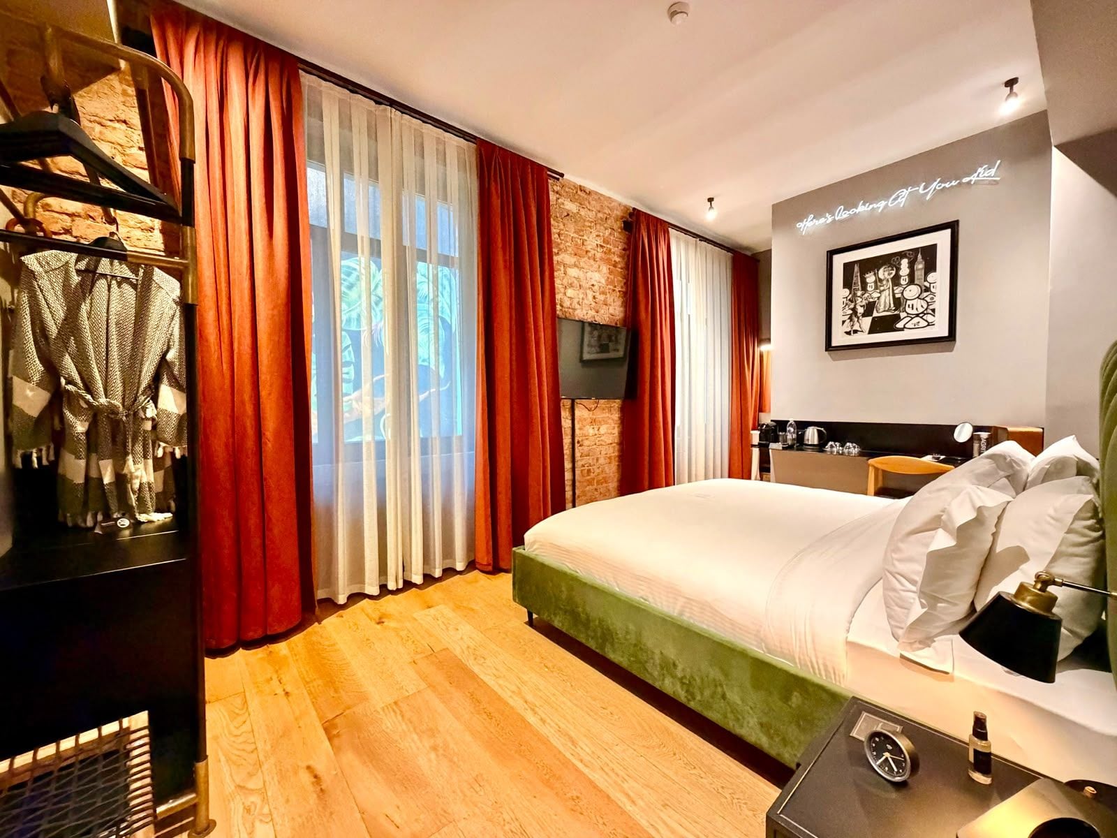 A hotel room with a bed, a desk, a chair, a clock, and a wall-mounted picture.
