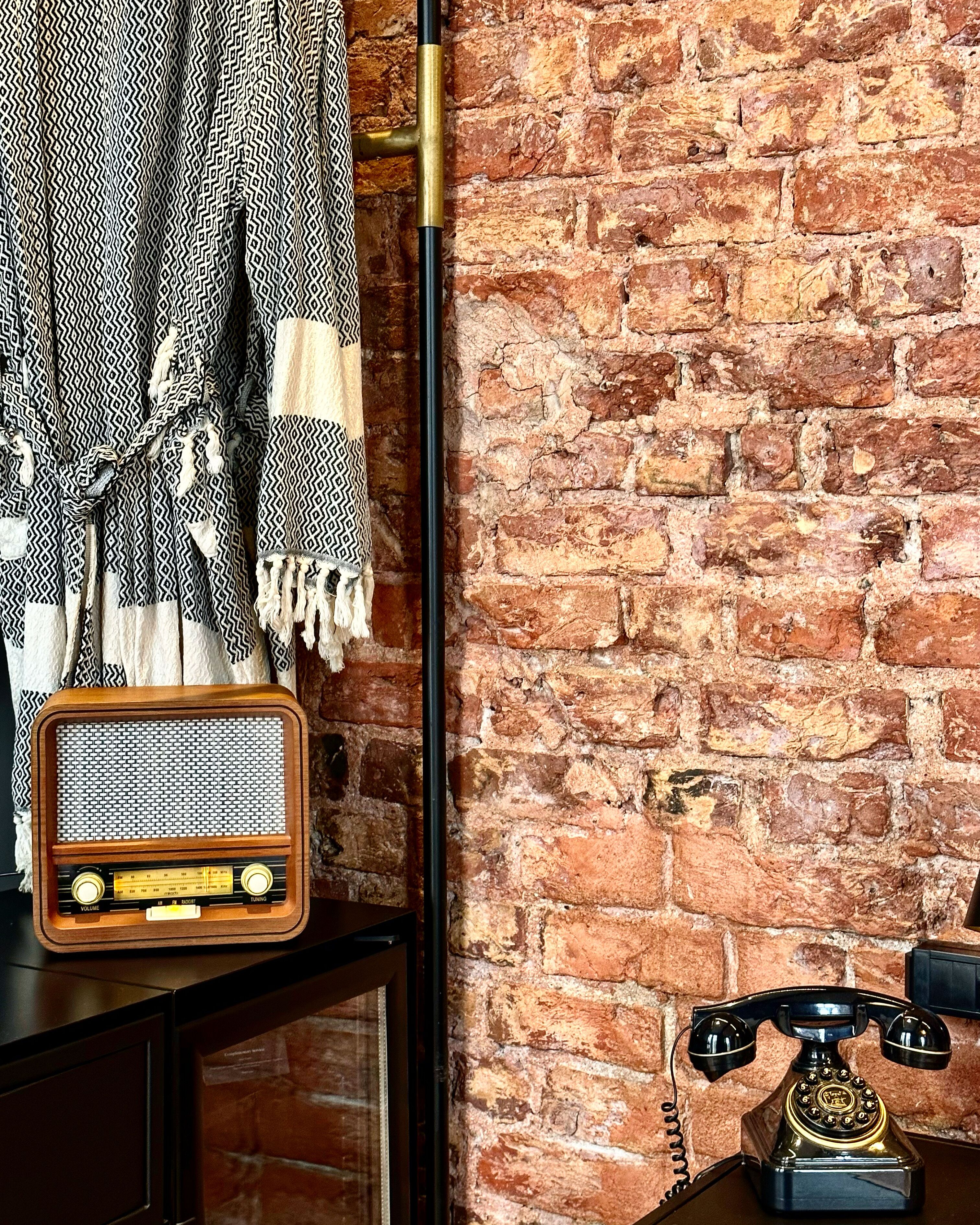 A vintage radio and telephone on a wooden surface against a brick wall.
