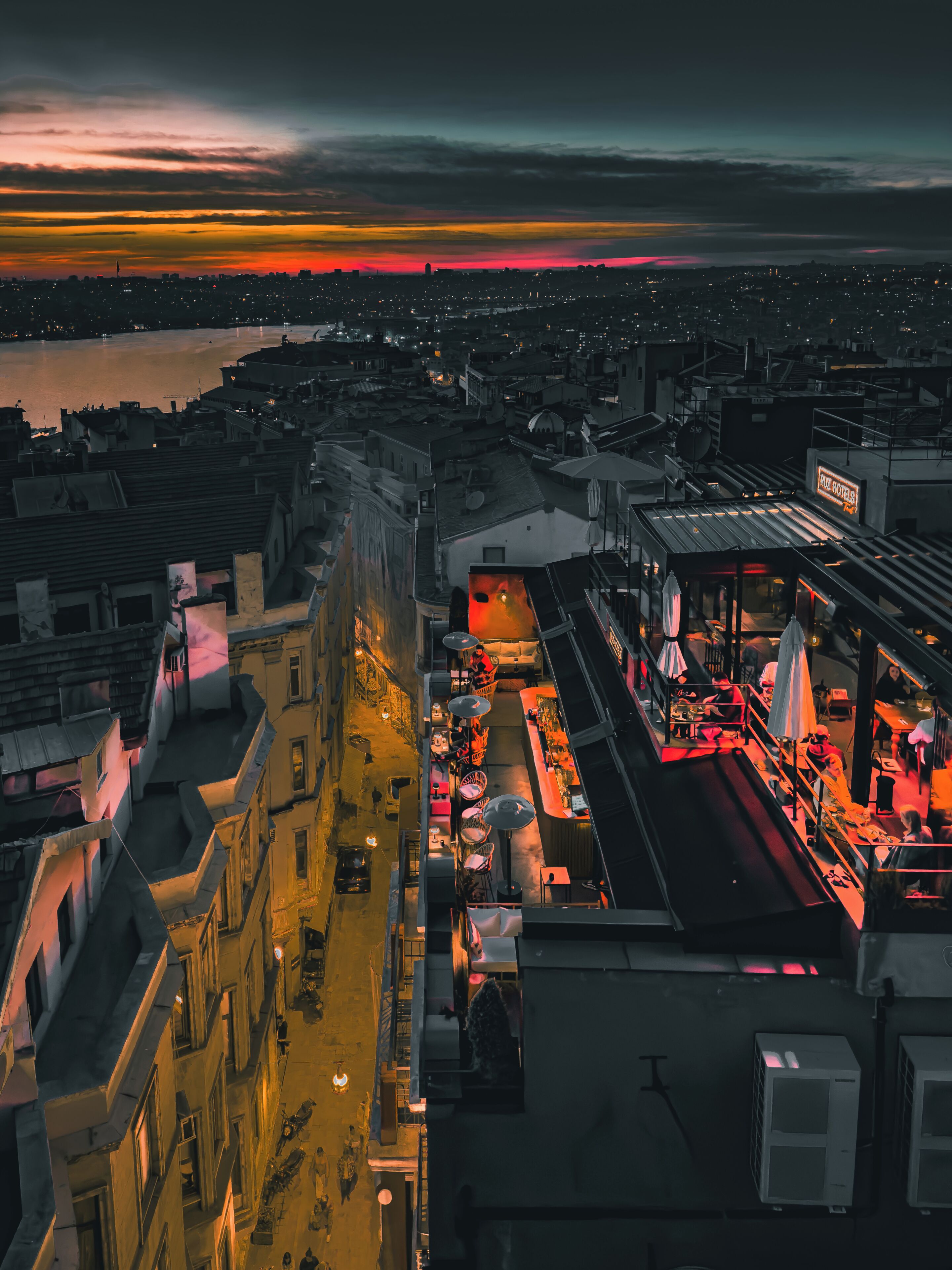A rooftop bar with outdoor seating and a view of the cityscape at dusk.