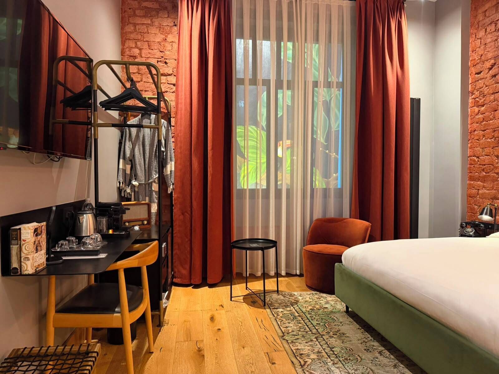 A hotel room with a bed, a desk with a chair, a small table, a TV, and a wardrobe.