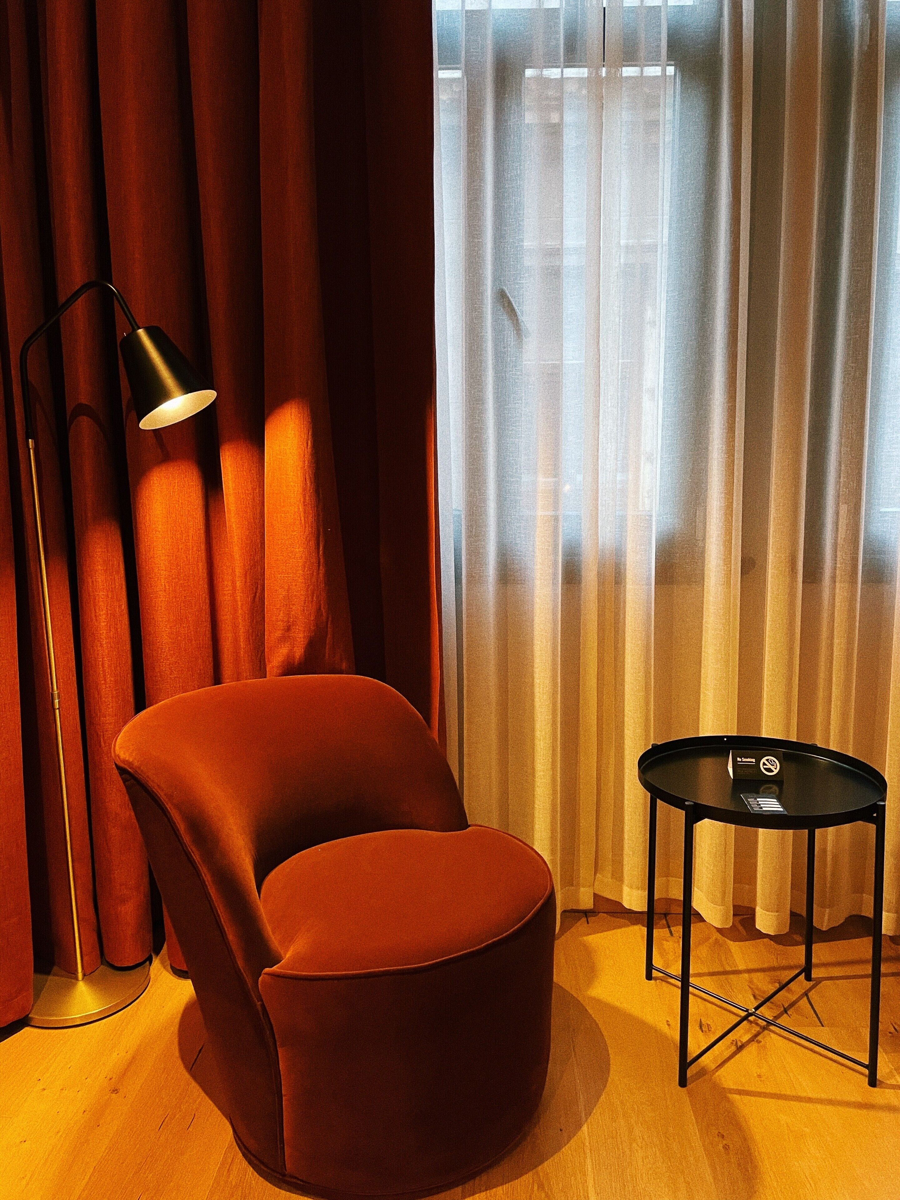 A room with a red velvet armchair, a black floor lamp, and a small black table with a white sign.