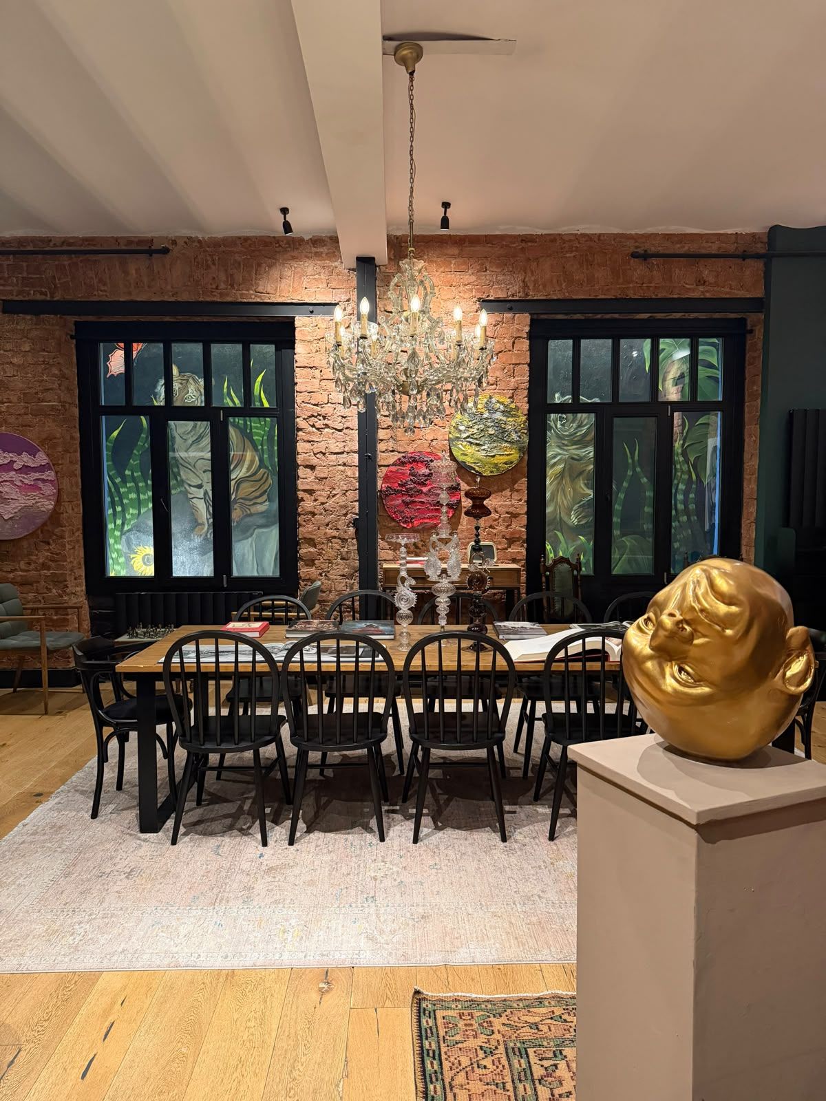 A dining area with a brick wall, large windows, a chandelier, and a unique golden sculpture.
