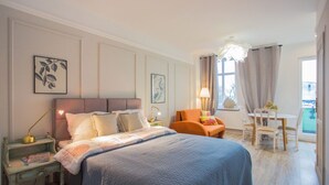 Une chambre à coucher avec un grand lit, une table de chevet, une chaise, une table et une fenêtre avec des rideaux.