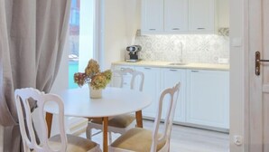 Un coin repas avec une table ronde et quatre chaises, une cuisine en arrière-plan et une grande fenêtre avec des rideaux.