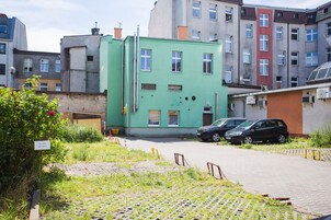 Un edificio verde con varias ventanas, un camino de entrada pavimentado y coches aparcados.