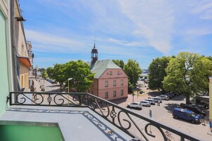 A street view with a building featuring a clock tower, parked cars, and trees.