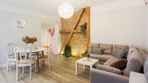 Un salon moderne avec un mur en briques, des poutres en bois, un lustre rond, un canapé gris et une table à manger avec des chaises.