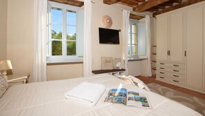 A bedroom with a bed, a bedside table, a TV, a wardrobe, and a window with curtains.
