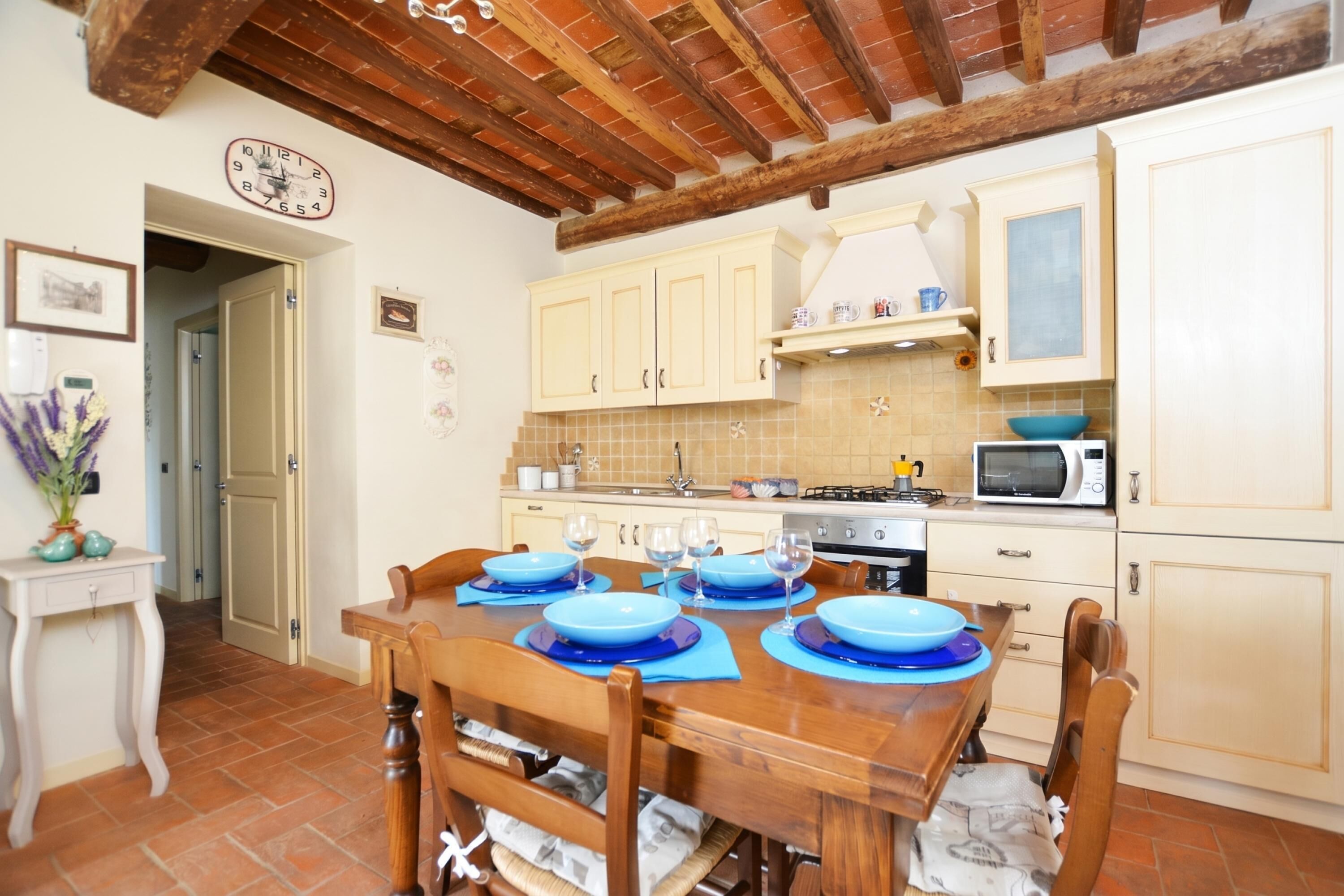 A kitchen with wooden cabinets, a dining table set with blue plates, and a clock on the wall.