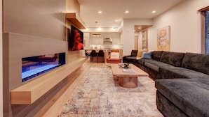 Un salon moderne doté d’un grand téléviseur à écran plat, d’un canapé de couleur foncée, d’une table basse en bois et d’un tapis à motifs.