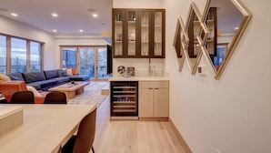 Un salon moderne comprenant un canapé, une table basse et un coin repas. La cuisine est équipée de placards et d’un lave-vaisselle. De grandes fenêtres laissent entrer la lumière naturelle et offrent une vue sur l’extérieur.