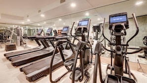 Une salle de sport équipée de tapis de course, de vélos elliptiques et d’un mur recouvert de miroirs.