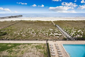 Une plage avec une jetée en bois, une piscine et un espace clos aménagé avec des chaises longues.