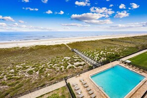 Une piscine avec des chaises longues, une vue sur la plage et un espace clos agrémenté de végétation.