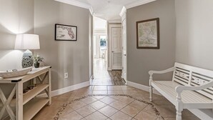 A hallway with a white bench, a table with a lamp, and two framed maps on the walls. - Spacious 3BR ocean-view condo, beautifully decorated! (Fernandina Beach)