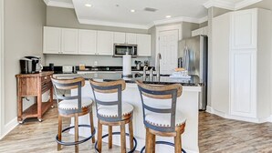 A modern kitchen with white cabinets, a stainless steel refrigerator, and a central island with bar stools. - Spacious 3BR ocean-view condo, beautifully decorated! (Fernandina Beach)