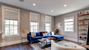 A spacious living room with a blue sectional sofa, a coffee table, and a white armchair. - Charming 3BR Uptown home with fenced yard. Walk to Magazine St, near streetcar & FQ. (New Orleans)