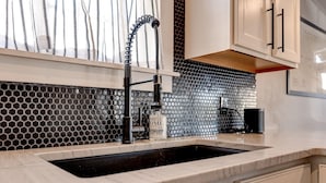 A kitchen with a black and white hexagonal backsplash, a stainless steel sink, and white cabinetry. - Charming 3BR Uptown home with fenced yard. Walk to Magazine St, near streetcar & FQ. (New Orleans)