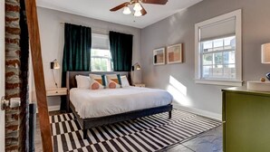A bedroom with a bed, a ceiling fan, a window with curtains, a bedside table, and a green dresser. - Charming 3BR Uptown home with fenced yard. Walk to Magazine St, near streetcar & FQ. (New Orleans)