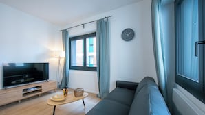 A modern living room with a flat-screen TV, a sofa, a small coffee table, and a window with curtains. - Boutique Apartment 2 (Lugano)