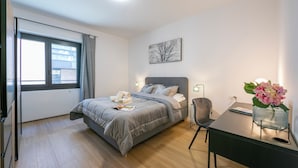 A modern bedroom with a bed, bedside table, desk, chair, and a window with curtains. - Boutique Apartment 3 (Lugano)