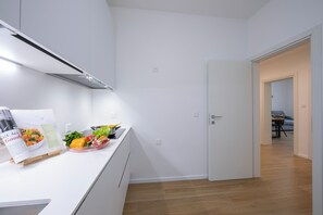 A modern kitchen with white cabinetry, a built-in stove, and a countertop with a recipe book and fresh vegetables. - Boutique Apartment 3 (Lugano)