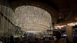 A bar with a large, ornate chandelier, shelves of liquor bottles, and several bar stools. - ON THE STRIP! | Classic Comfort - 2 Bedroom Condo (Las Vegas)