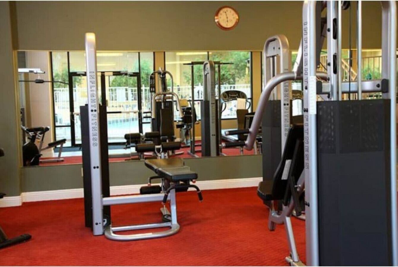 A gym with various exercise equipment, a clock on the wall, and large windows.