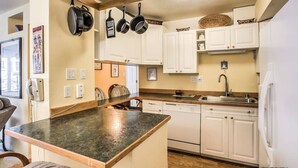 A kitchen with white cabinets, a granite countertop, and hanging pots. - ON THE STRIP! | Classic Comfort - 2 Bedroom Condo (Las Vegas)