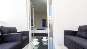 Een balkon met rieten meubilair, een glazen tafel en een bed op de achtergrond.