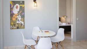 Een eetgedeelte met een ronde tafel en vier witte stoelen, een wandlamp en een kleurrijk abstract schilderij.