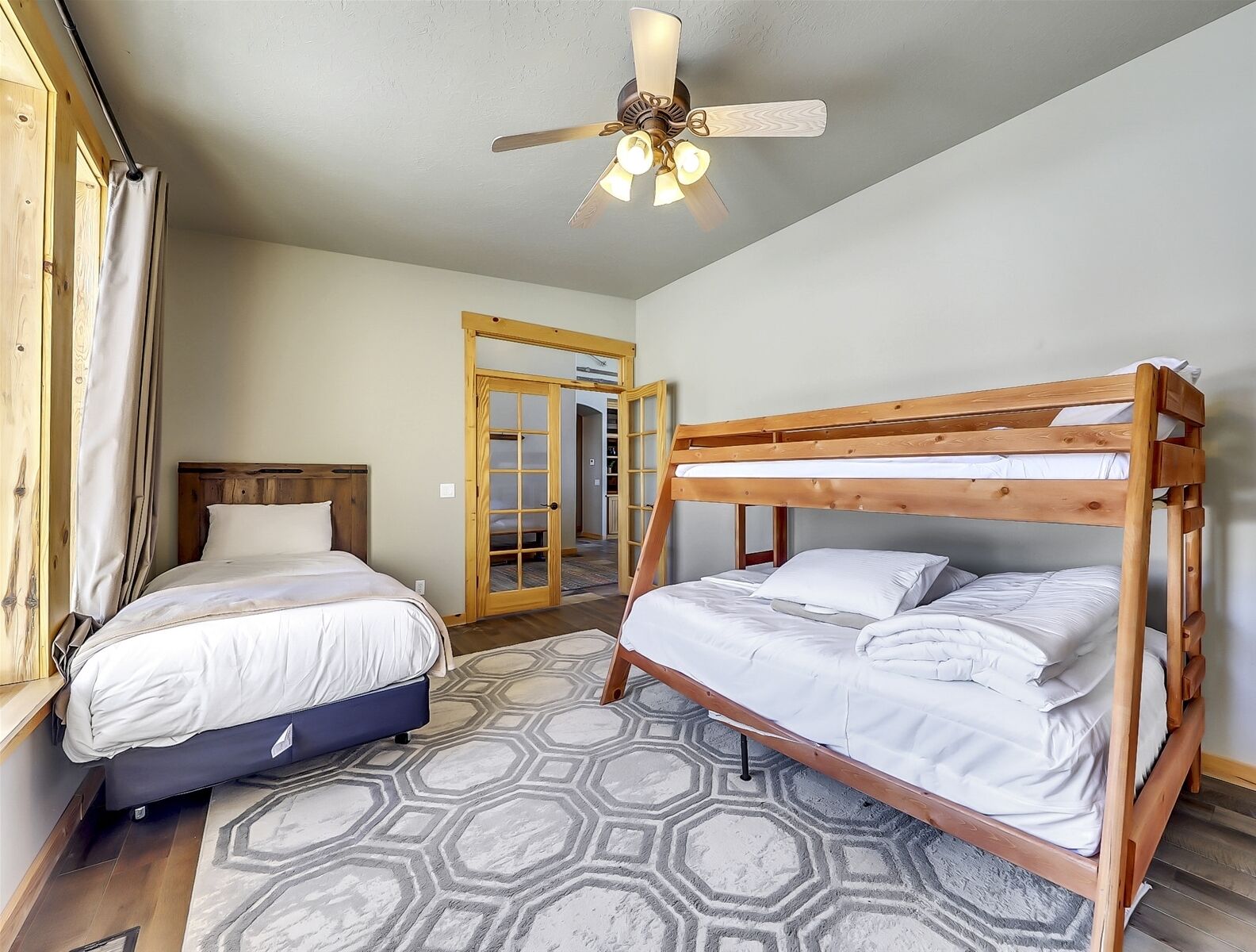 A bedroom with a bunk bed, a single bed, a ceiling fan, and a geometric-patterned rug.