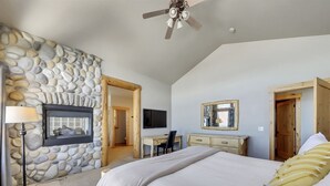 Une chambre avec un mur en pierre, un lit, un bureau, une chaise, un téléviseur et un ventilateur de plafond.