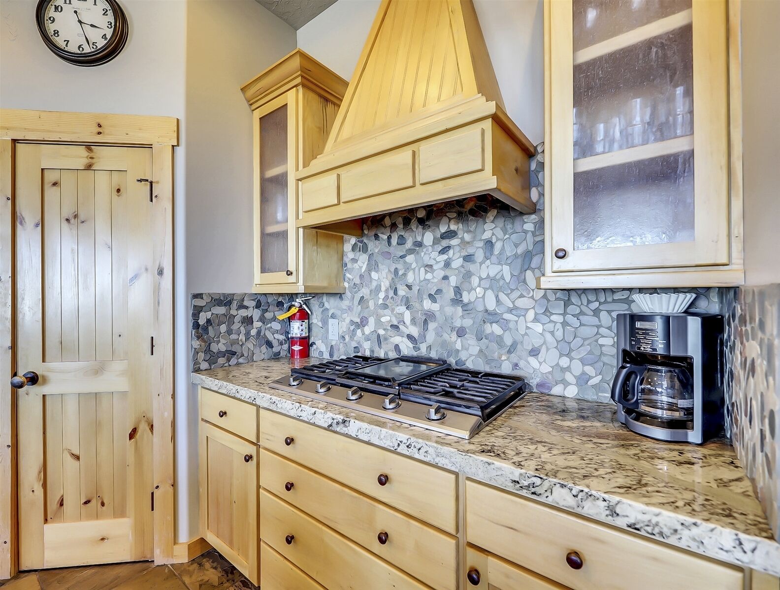 A kitchen with wooden cabinets, a stone backsplash, a gas stove, and a coffee maker.