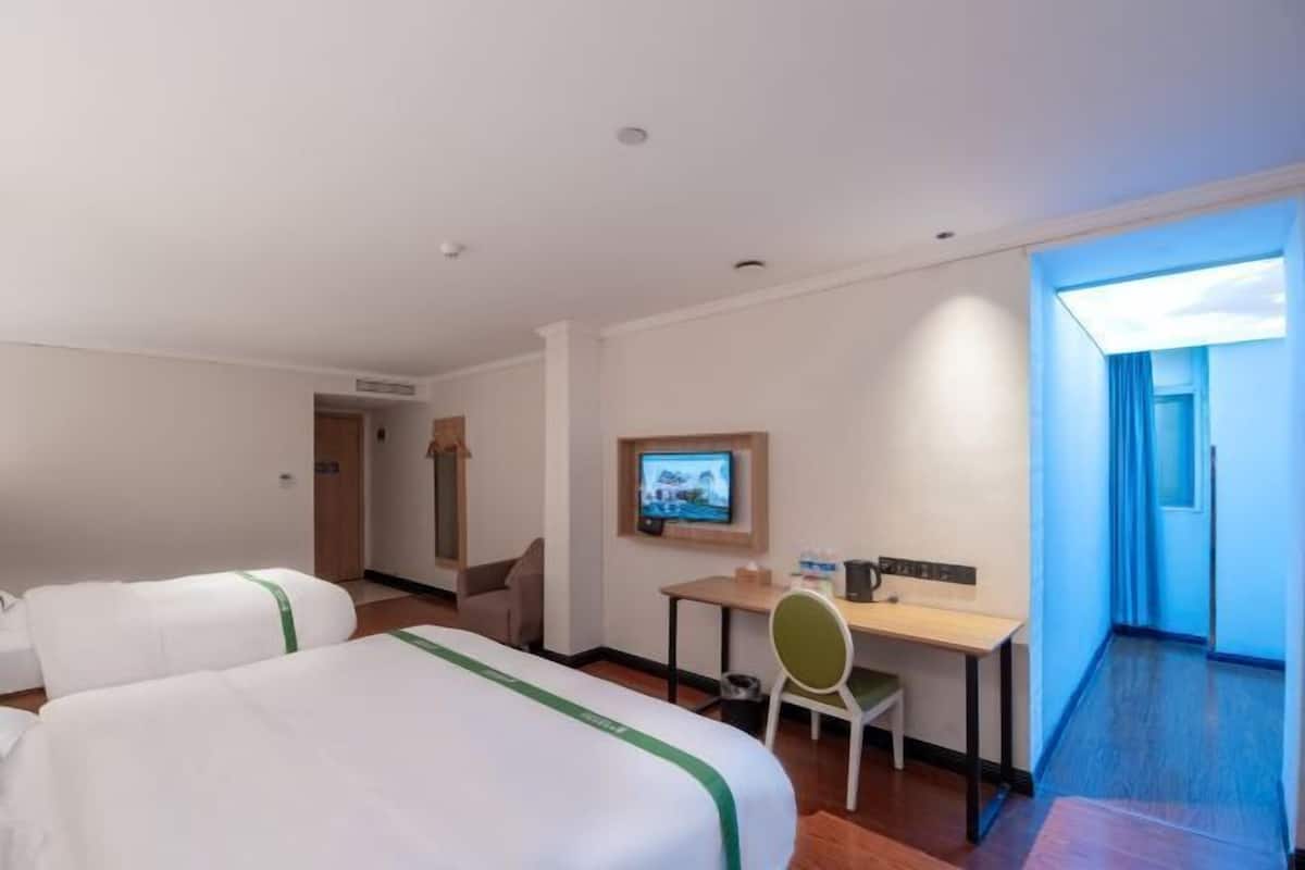 A hotel room with two beds, a desk, a television, and a view of the outside.