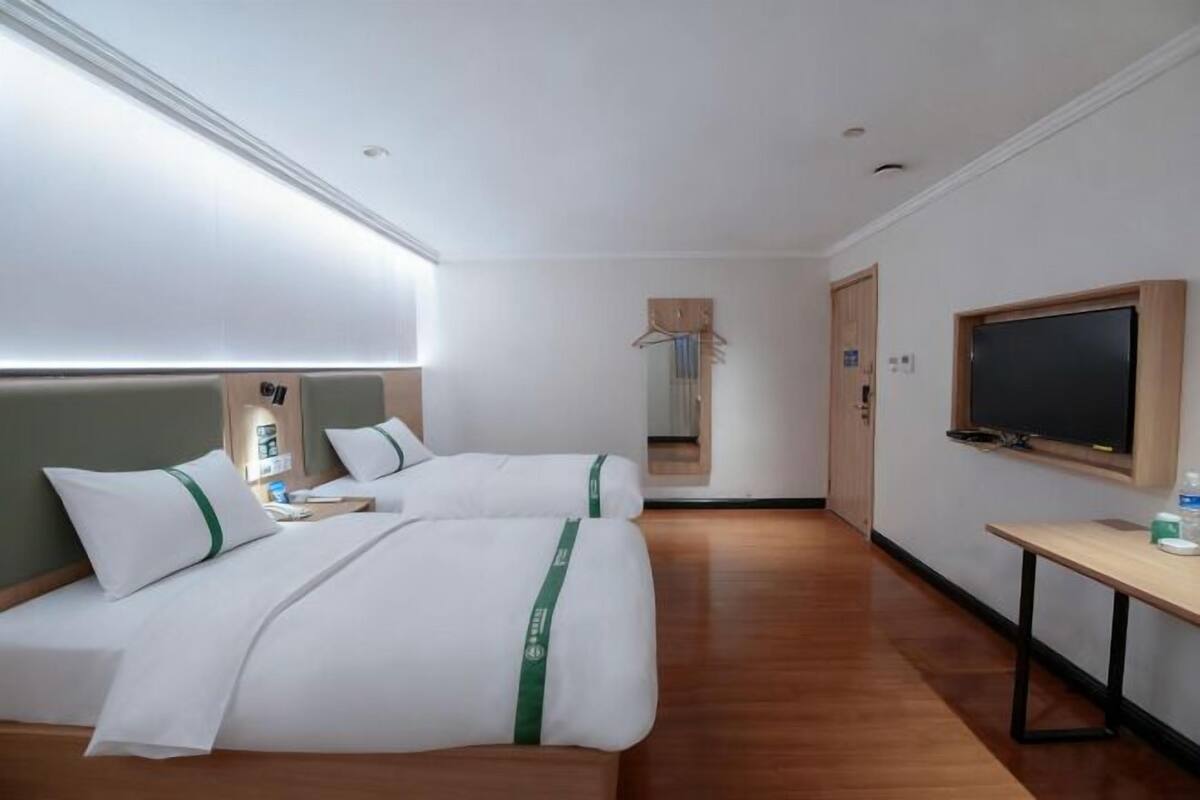 A hotel room with two beds, a TV, a desk, and a mirror.
